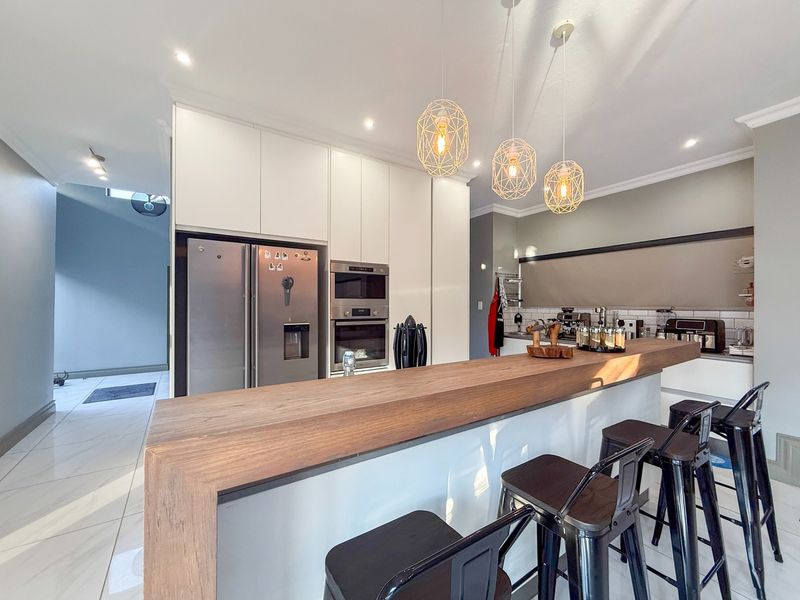 Modern kitchen featuring sleek white cabinetry, a substantial timber-topped breakfast bar, built-in appliances, and stylish pendant lighting over the workspace.
