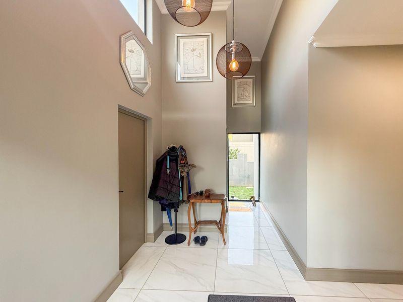 A bright and spacious entrance hall featuring high ceilings, modern tiled flooring, and natural light from a skylight and rear glass door.