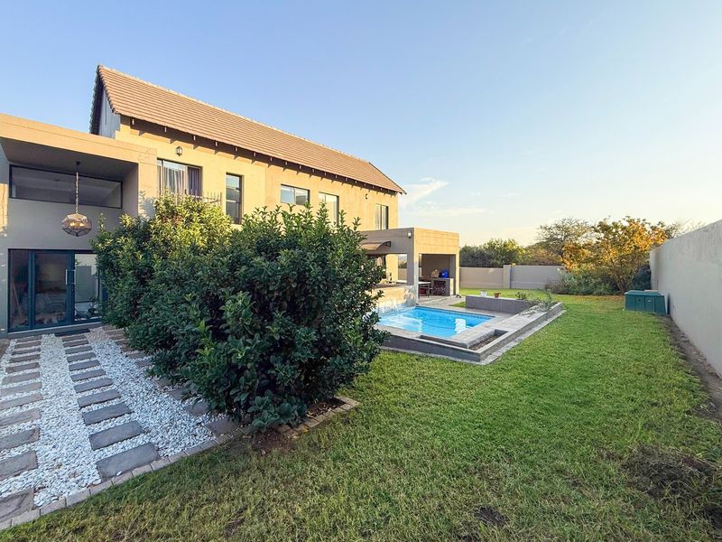 Rear view of the property featuring a well-maintained garden, a swimming pool, and a covered patio area with a built-in braai.