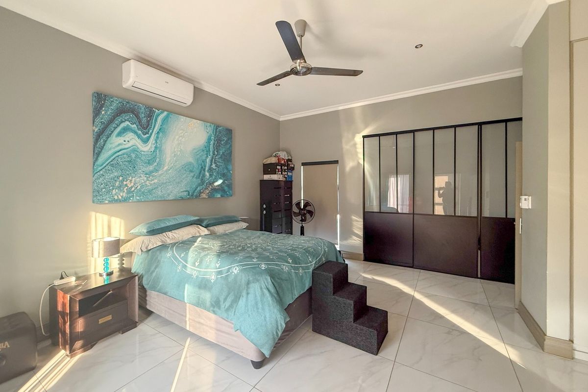 Spacious bedroom featuring large-format tiled flooring, a modern ceiling fan, split-system air conditioning, and extensive built-in wardrobe storage with dark framed glass doors.