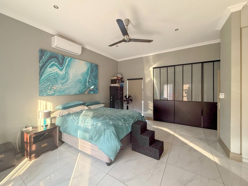 Spacious bedroom featuring large-format tiled flooring, a modern ceiling fan, split-system air conditioning, and extensive built-in wardrobe storage with dark framed glass doors.