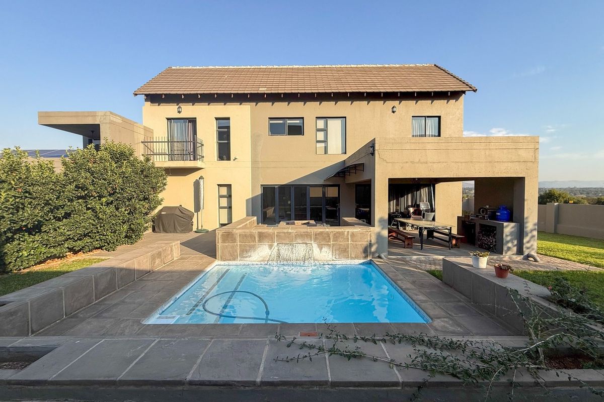 Rear view of the house featuring a swimming pool with a water feature, a covered patio with a built-in braai, and a balcony.