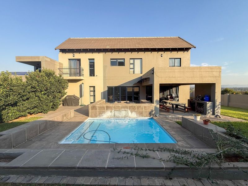 Rear view of the house featuring a swimming pool with a water feature, a covered patio with a built-in braai, and a balcony.