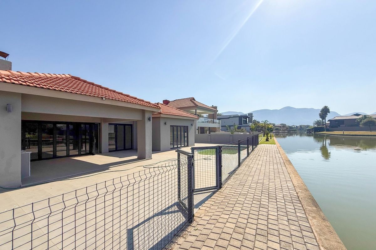 Rear view of the property featuring a covered patio, paved waterfront walkway, and direct access to the canal.