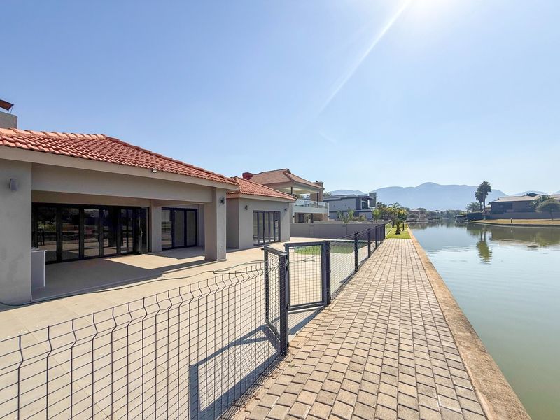 Rear view of the property featuring a covered patio, paved waterfront walkway, and direct access to the canal.