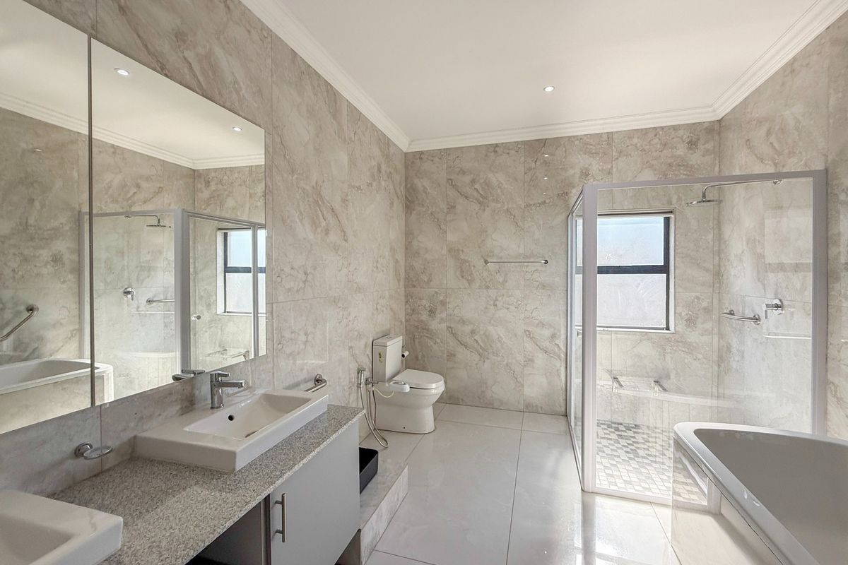 Modern, spacious bathroom featuring a double vanity with stone countertop, a glass-enclosed shower, a freestanding bathtub, and elegant floor-to-ceiling marble-look tiling.