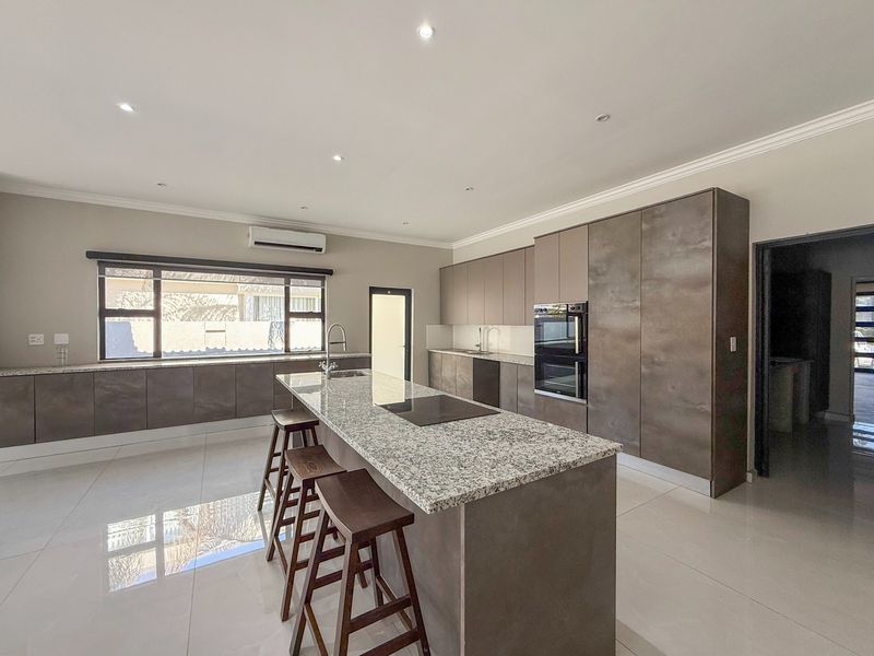 Modern kitchen featuring a large granite-topped island, built-in appliances, sleek cabinetry, and polished tiled flooring with recessed lighting.