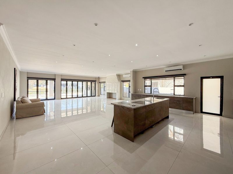Spacious open-plan living area featuring a modern kitchen with a central island, sleek cabinetry, fireplace, and large stacking doors leading to the outdoors.