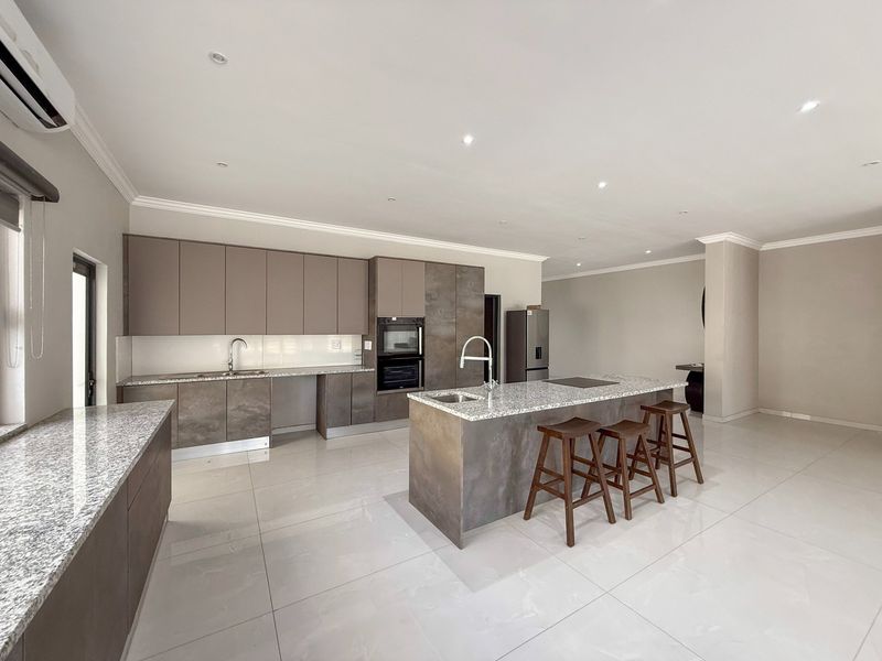 Modern open-plan kitchen featuring sleek cabinetry, granite countertops, a central island with seating, and high-quality built-in appliances.