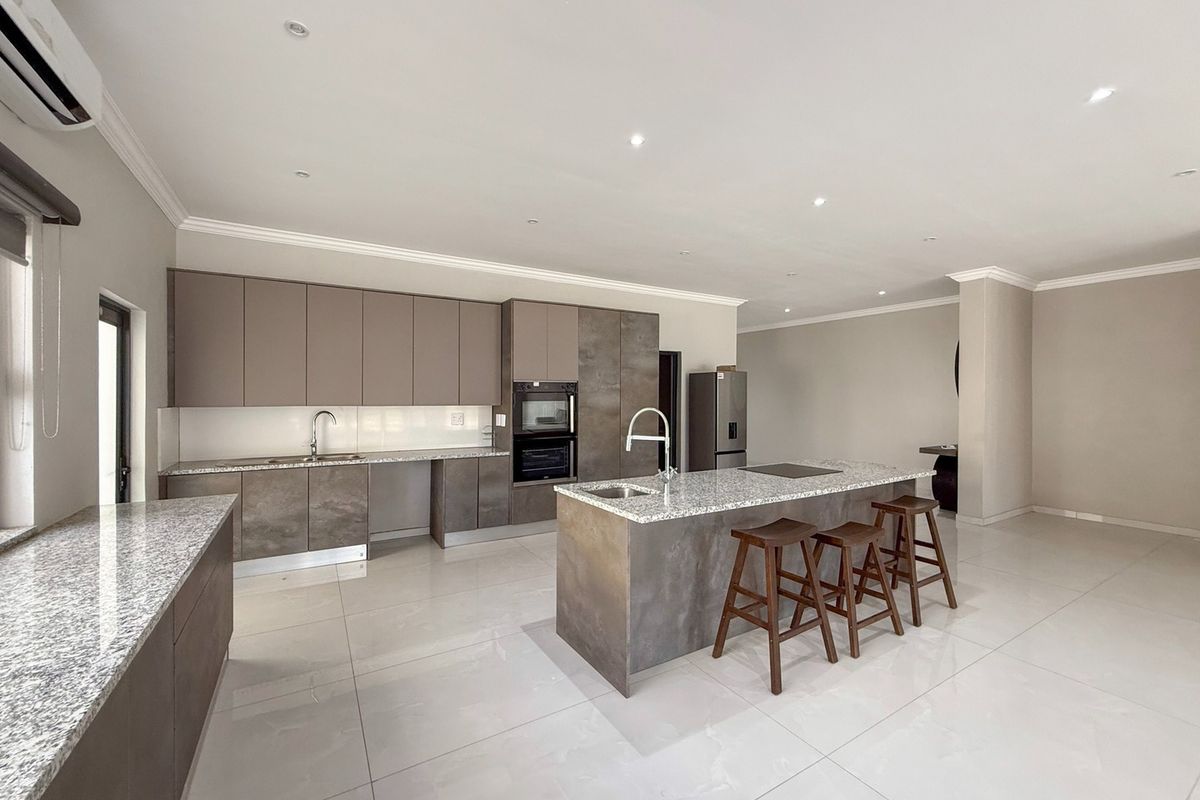 Modern open-plan kitchen featuring sleek cabinetry, granite countertops, a central island with seating, and high-quality built-in appliances.