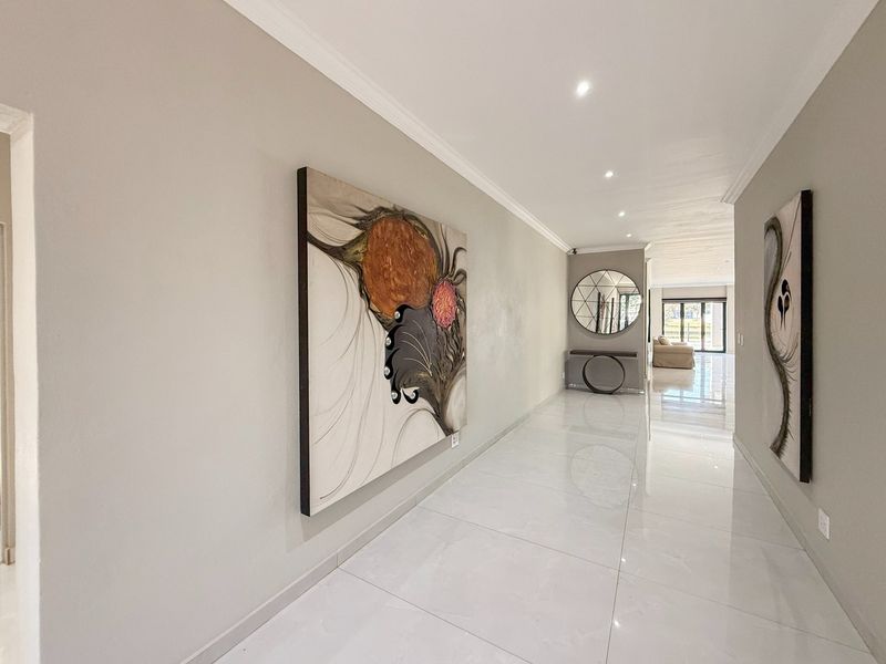 A bright and spacious hallway featuring polished porcelain tile flooring, recessed downlighting, and clean, neutral wall finishes leading toward the main living area.