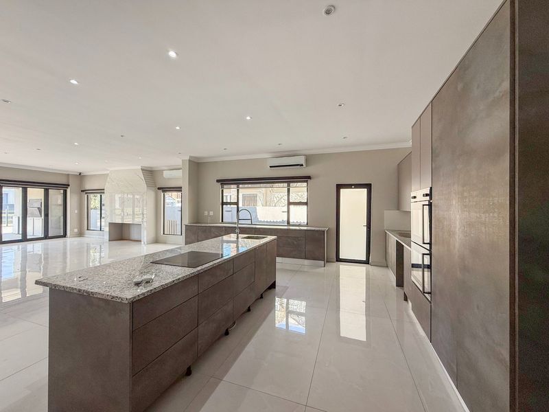Spacious open-plan kitchen and living area featuring a large island with granite countertops, built-in appliances, sleek cabinetry, and polished tiled flooring throughout.