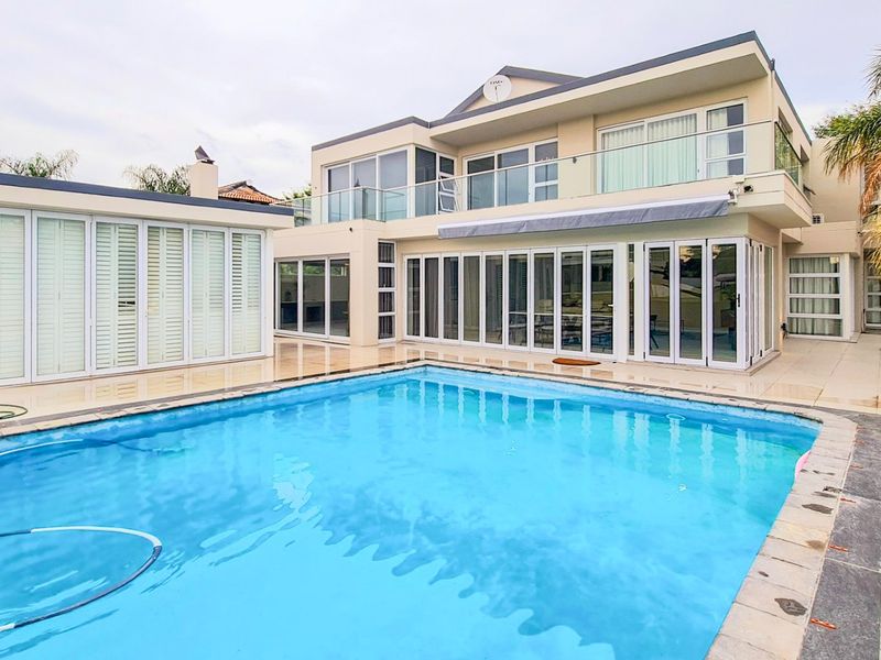 A modern rear exterior view featuring a swimming pool, expansive folding glass doors, and upper-level balconies with glass balustrades.