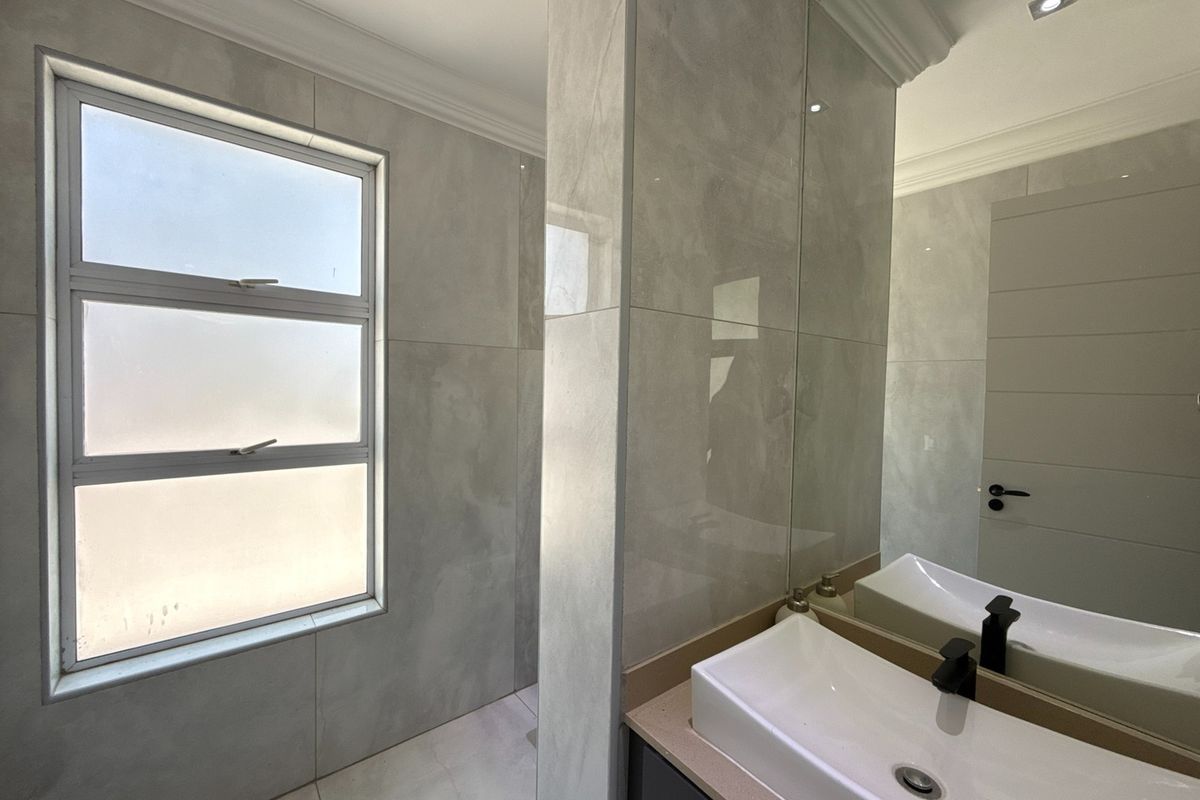 Modern bathroom featuring large format grey wall tiles, a sleek vanity with a vessel sink, a large mirror, and a frosted window for privacy.