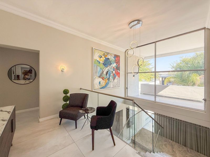 A bright and modern landing area featuring a sleek glass balustrade, large windows providing natural light, and contemporary pendant lighting.