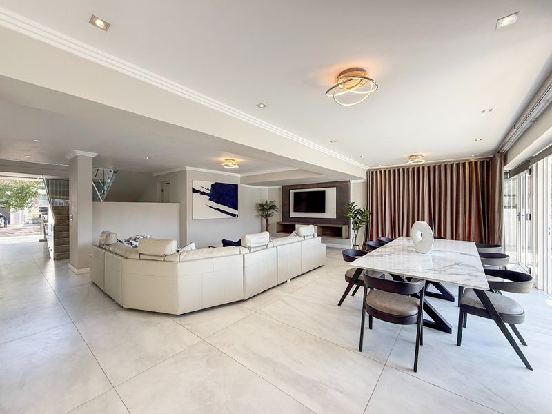 Spacious open-plan living and dining area featuring large format floor tiles, recessed lighting, and a modern built-in media unit with seamless outdoor access.