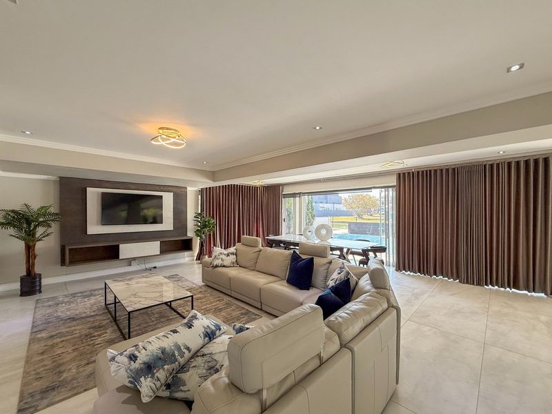 Spacious living room featuring large sliding glass doors, built-in media console, recessed lighting, and neutral tiled flooring with a seamless flow to the outdoors.