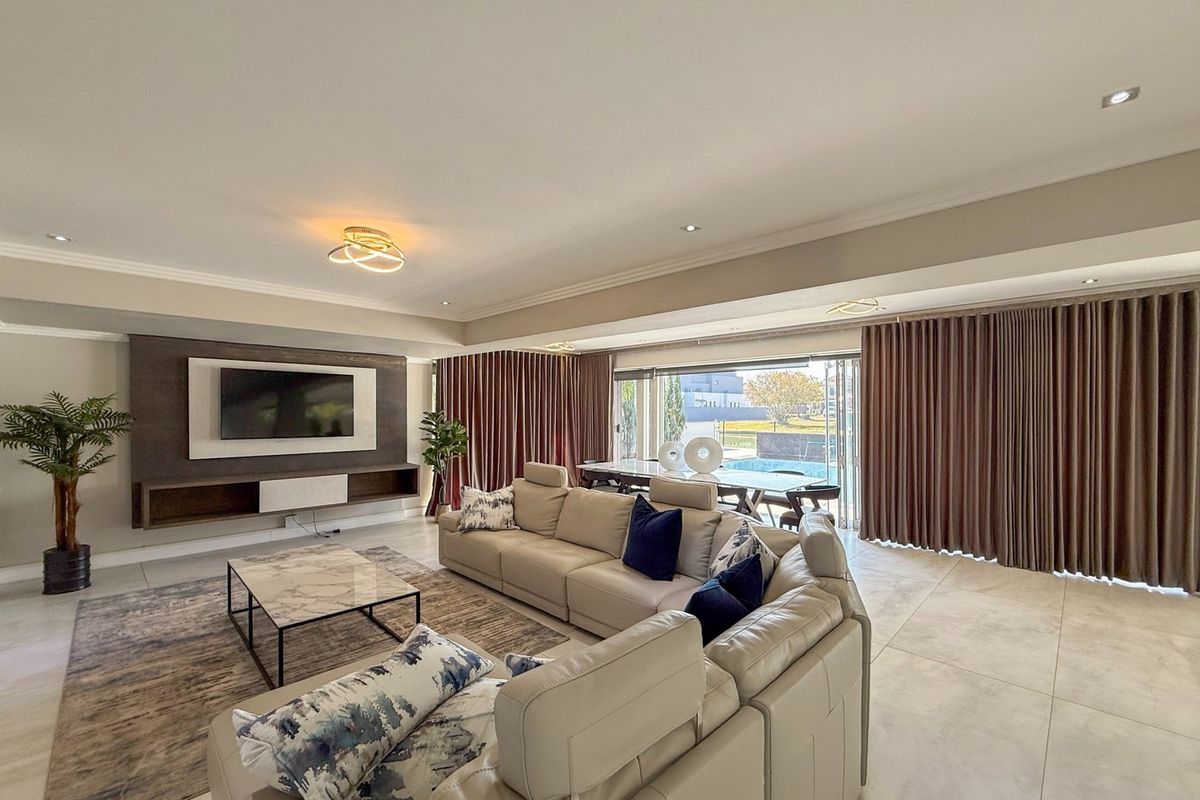 Spacious living room featuring large sliding glass doors, built-in media console, recessed lighting, and neutral tiled flooring with a seamless flow to the outdoors.