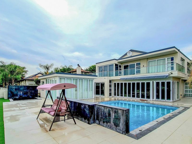 Rear exterior view featuring a swimming pool, tiled patio area, modern glass folding doors, and a built-in water feature.