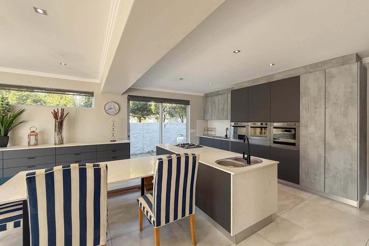 Modern open-plan kitchen featuring a central island with stone countertops, integrated appliances, sleek cabinetry, and direct access to the outdoor area.