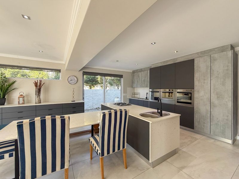 Modern open-plan kitchen featuring a central island with stone countertops, integrated appliances, sleek cabinetry, and direct access to the outdoor area.