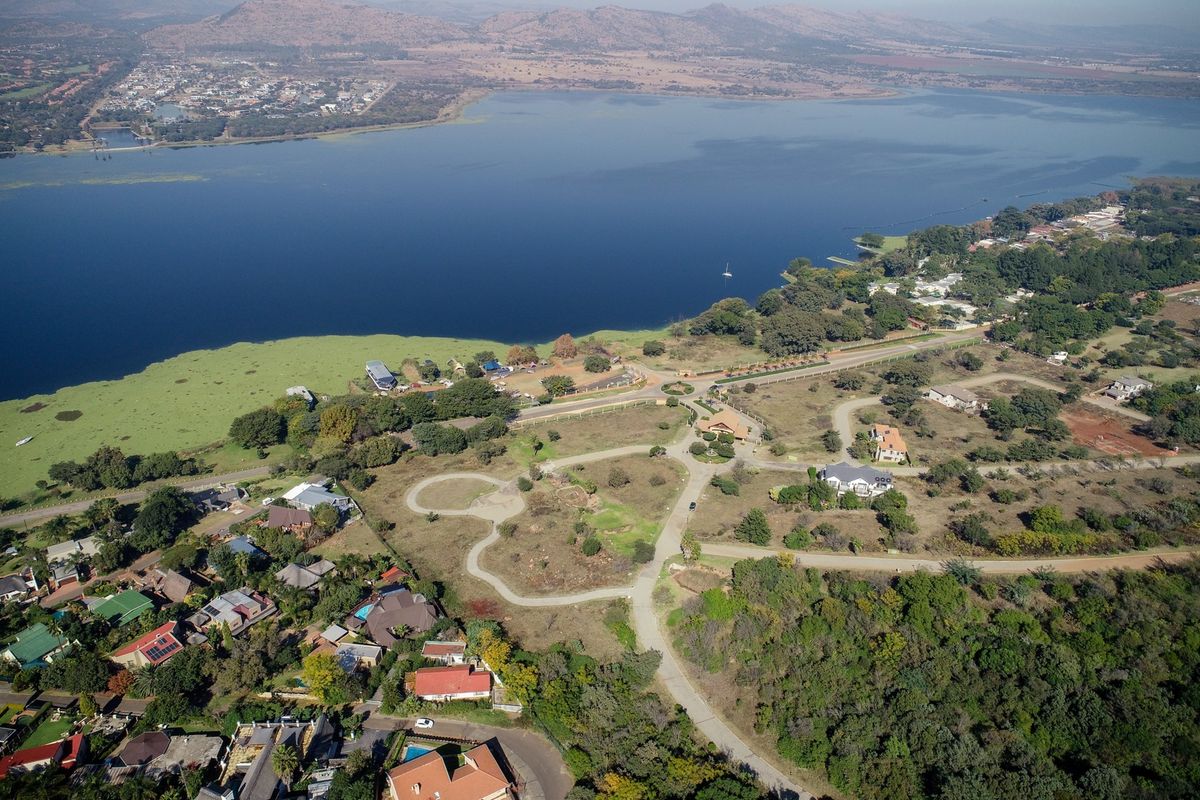An aerial view of a residential estate featuring paved roads, established vegetation, and direct access to a large lake.