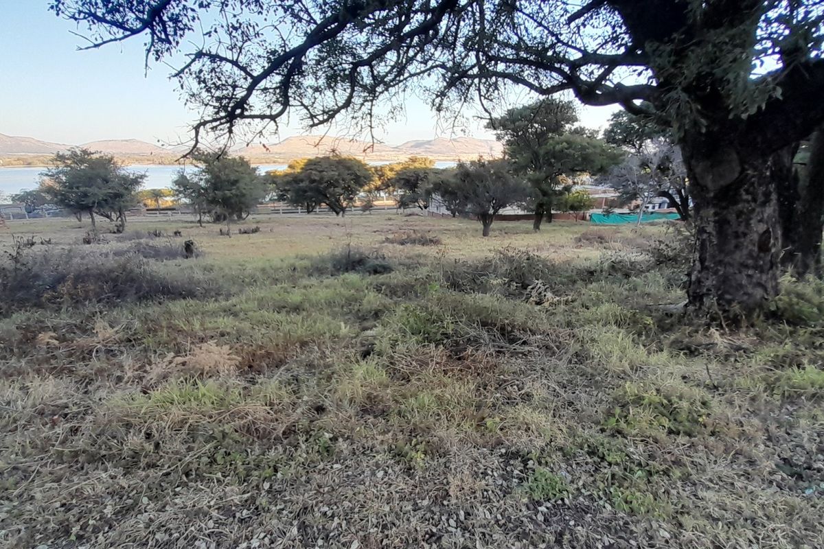 A scenic view of the vacant residential land featuring mature trees and a gentle slope, overlooking the distant lake and mountain landscape.