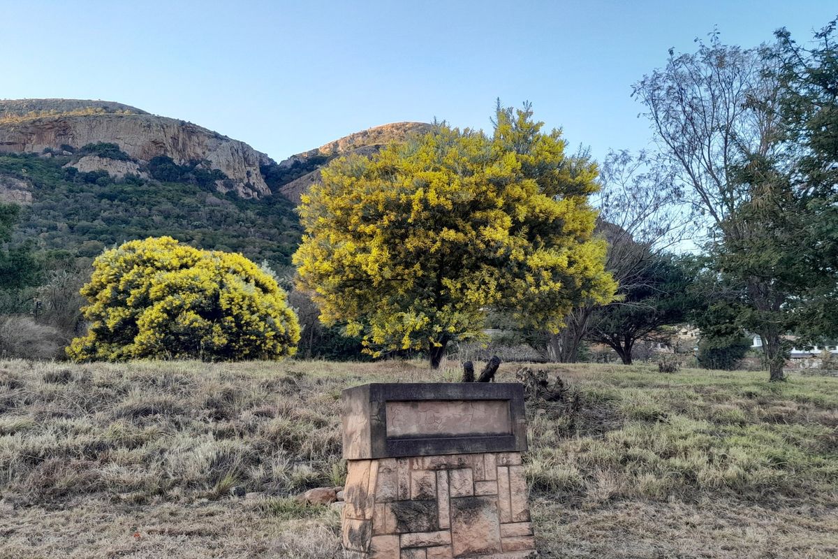 A scenic view of a vacant residential plot featuring a stone pillar structure set against a backdrop of natural vegetation and mountain terrain.