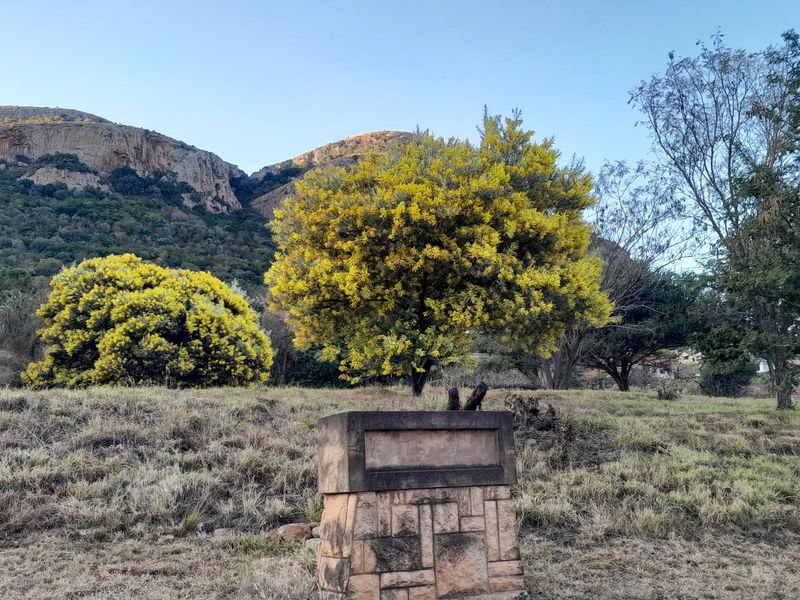 A scenic view of a vacant residential plot featuring a stone pillar structure set against a backdrop of natural vegetation and mountain terrain.