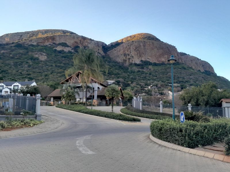 A view of the residential estate entrance featuring paved roads, perimeter fencing, and scenic mountain views in the background.