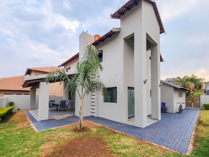 Rear view of a modern double-story house featuring a covered patio, paved outdoor area, and a well-maintained garden.