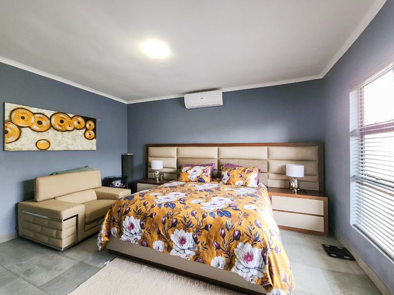 A well-maintained bedroom featuring tiled flooring, a built-in headboard with integrated bedside tables, and a wall-mounted air conditioning unit.
