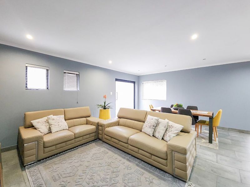 Spacious open-plan living and dining area featuring neutral grey walls, tiled flooring, and recessed downlighting with natural light from multiple windows.