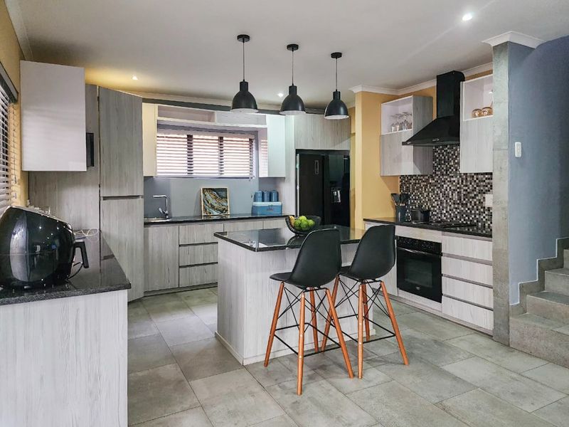 Modern kitchen featuring a central island, granite countertops, built-in oven with extractor fan, and stylish mosaic tile backsplash with ample cabinetry.