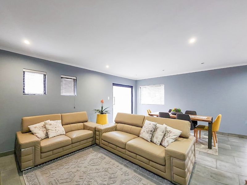 Spacious open-plan living and dining area featuring neutral grey walls, tiled flooring, and recessed downlighting, creating a bright and functional living space.