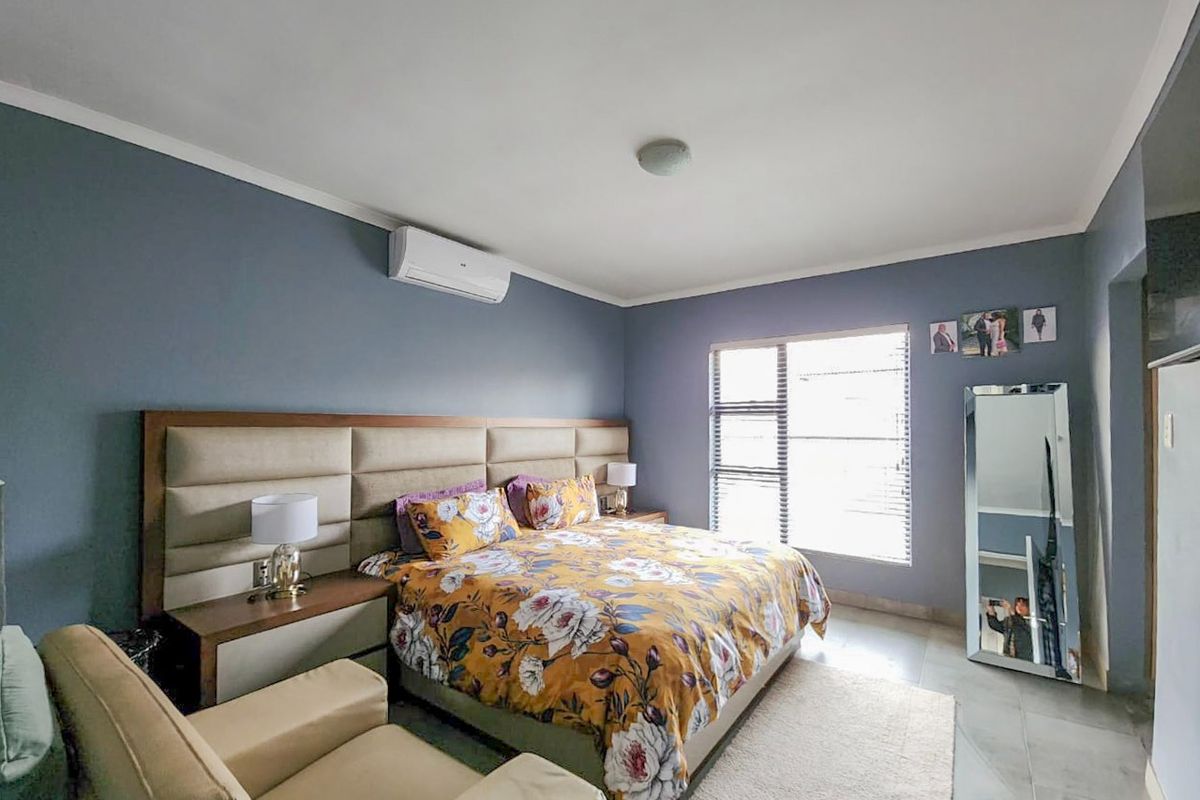 A well-maintained bedroom featuring tiled flooring, a built-in headboard, and a wall-mounted split-system air conditioner.