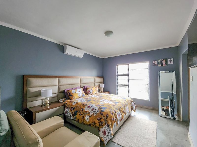 A well-maintained bedroom featuring tiled flooring, a built-in headboard, and a wall-mounted split-system air conditioner.