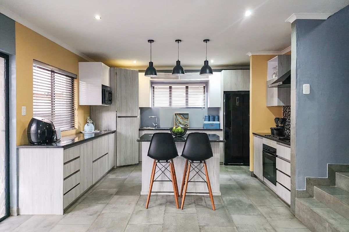 Modern kitchen featuring a central island, stone countertops, built-in oven, extractor fan, and contemporary cabinetry with recessed and pendant lighting.