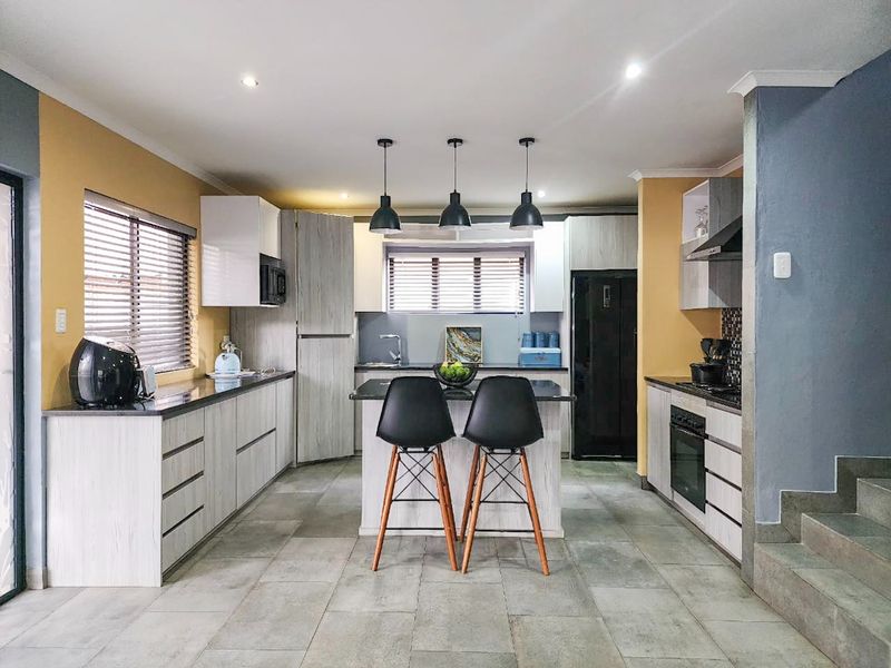 Modern kitchen featuring a central island, stone countertops, built-in oven, extractor fan, and contemporary cabinetry with recessed and pendant lighting.