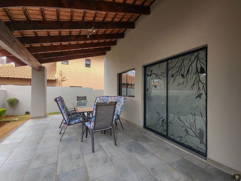 A covered patio area featuring exposed timber beams, tiled flooring, and a large sliding glass door with decorative frosted detailing.
