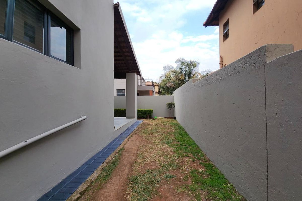 A side garden pathway featuring a boundary wall, paved drainage channel, and access to the rear patio area.