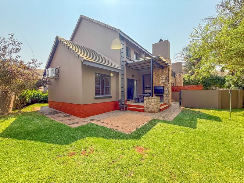 Rear view of the townhouse featuring a paved patio area with a built-in braai, stone cladding accents, and a well-maintained garden.