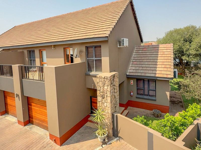 A well-maintained townhouse exterior featuring a tiled roof, stone cladding accents, a balcony, and a paved driveway with an integrated garage.