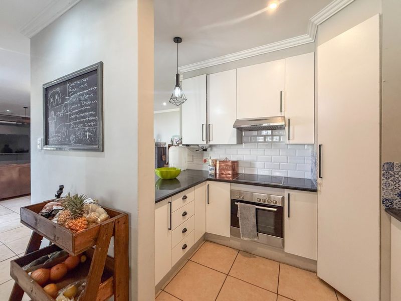 A compact, functional kitchen featuring white cabinetry, subway tile backsplash, stone countertops, and integrated stainless steel appliances.