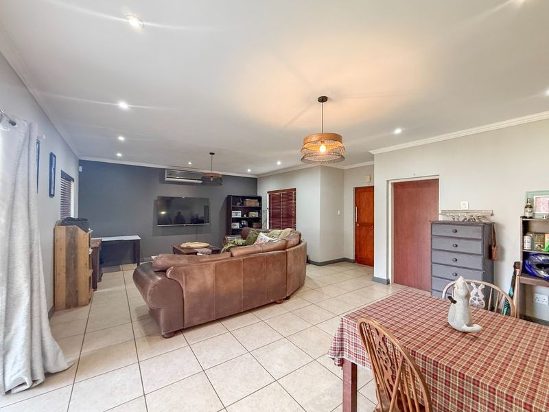 Spacious open-plan living and dining area featuring neutral tiled flooring, recessed lighting, and a split-system air conditioning unit.