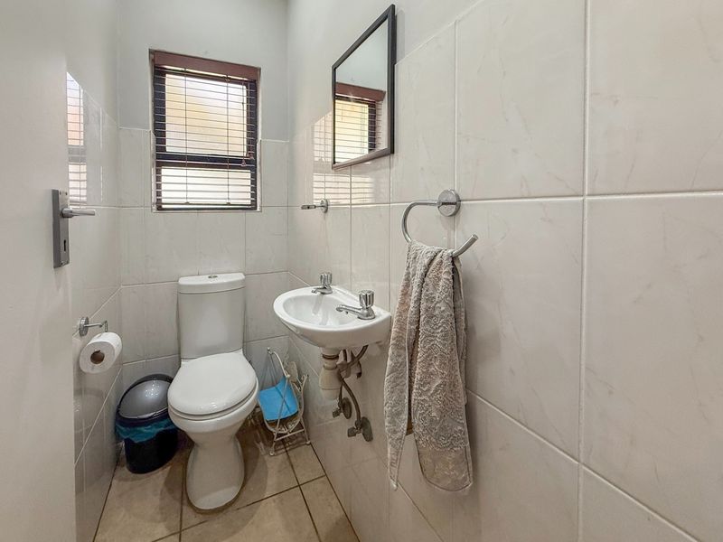 A compact guest bathroom featuring neutral ceramic wall and floor tiles, a wall-mounted basin, and a dual-flush toilet.