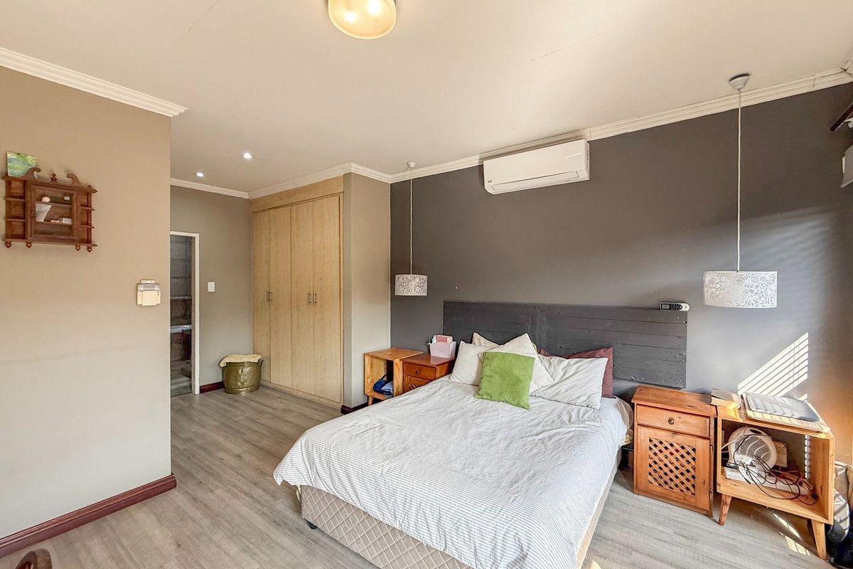 A well-maintained bedroom featuring laminate flooring, built-in cupboards, a split-system air conditioner, and modern pendant lighting.