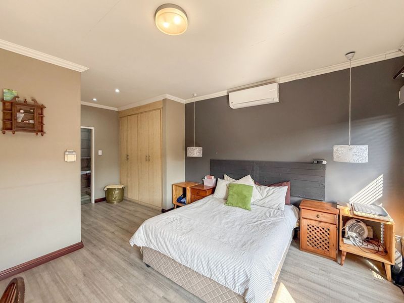 A well-maintained bedroom featuring laminate flooring, built-in cupboards, a split-system air conditioner, and modern pendant lighting.