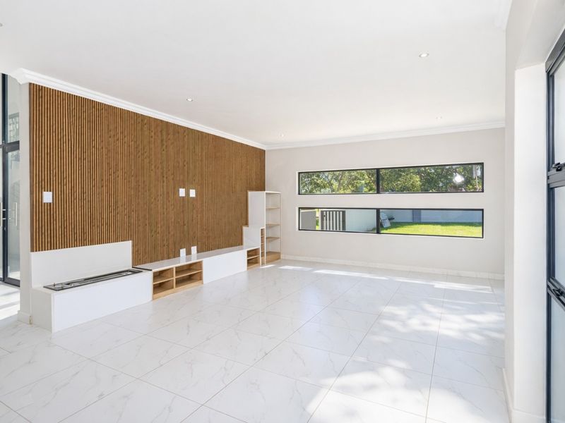 Spacious living area featuring a modern slatted timber feature wall, built-in media cabinetry, large porcelain floor tiles, and abundant natural light through expansive windows.