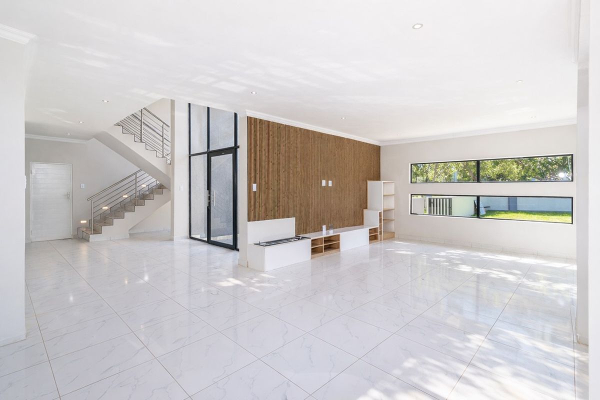 Spacious open-plan living area featuring modern porcelain tile flooring, a striking slatted timber feature wall, and a contemporary staircase with metal balustrades.